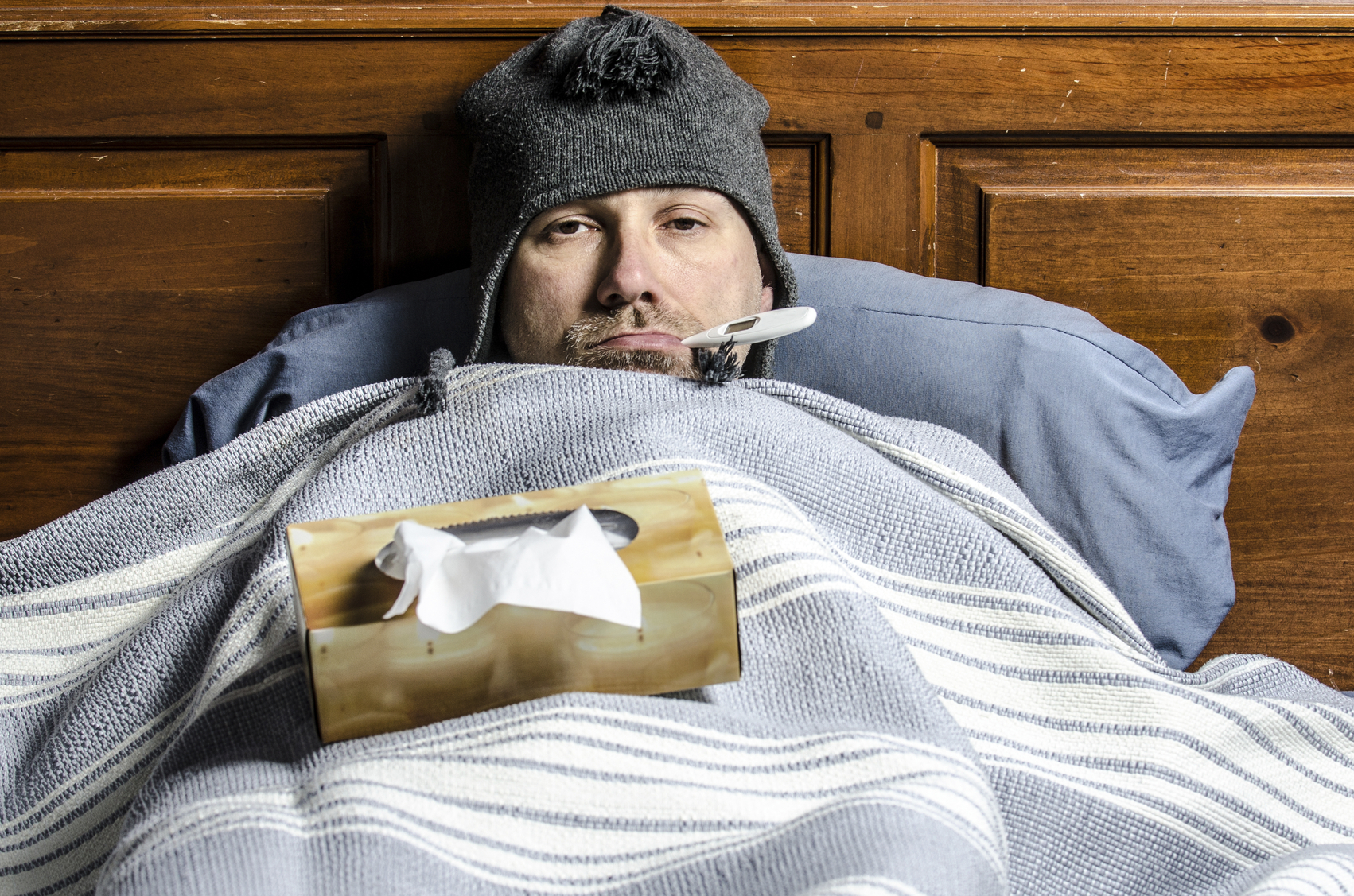 A man sick in bed with a thermometer in his mouth